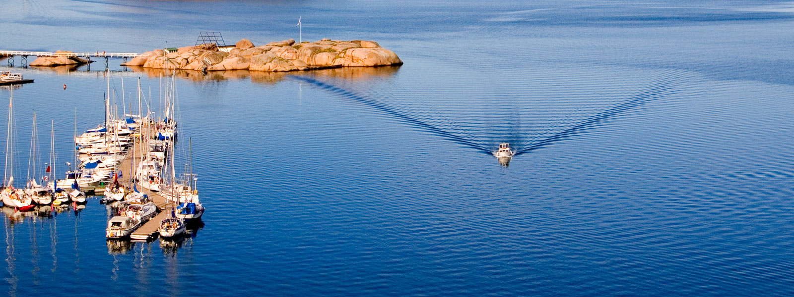boat on calm sea going past a small harbor